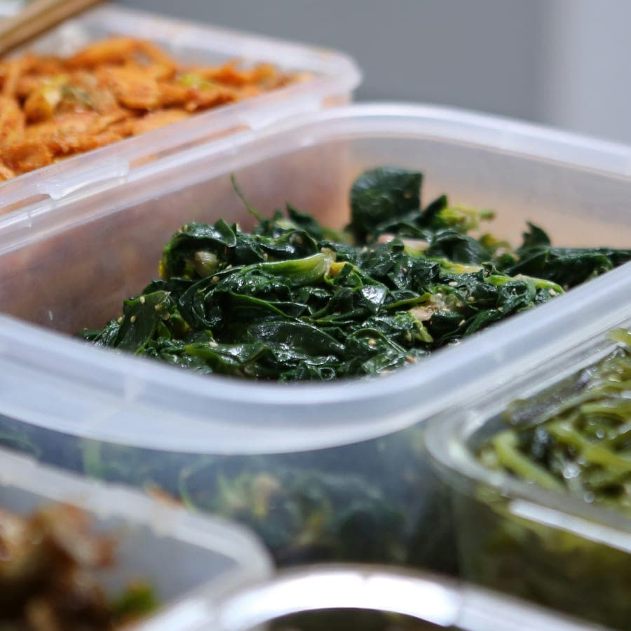 A container of sautéed greens among other portioned vegetable dishes.