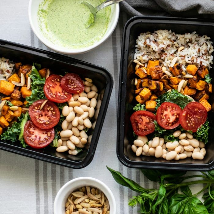 Two portioned containers of roasted sweet potato, kale, tomato and white beans over rice.