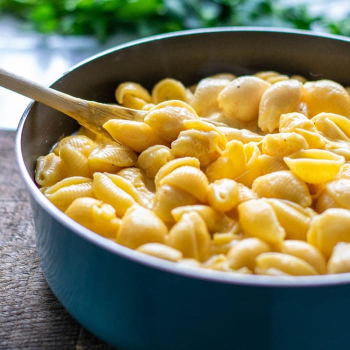 A pan of shell macaroni in cheese sauce with a wooden spoon.