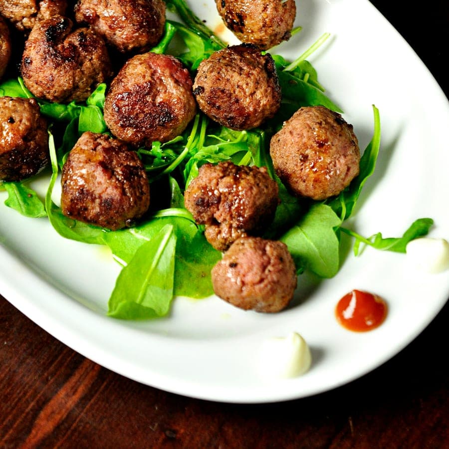 Browned meatballs on a bed of rocket on a white plate.